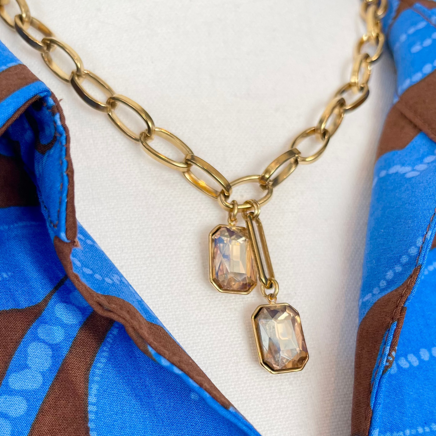 close up of Gold chain necklace with double-drop topaz crystal pendant on mannequin with blue and brown dress