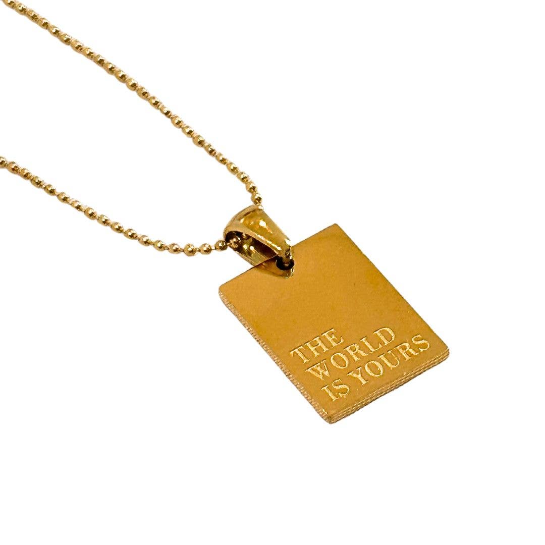 gold necklace with rectangular pendant with "The World is Yours" engraved on it