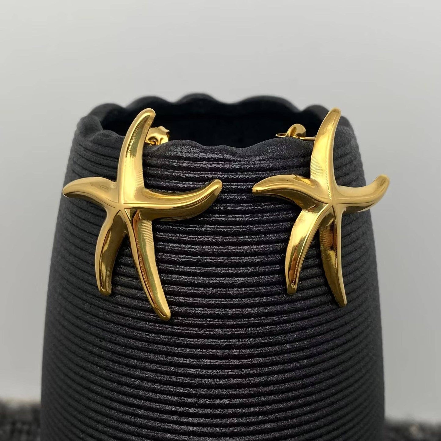a pair of gold starfish stud earrings hanging on a black vase