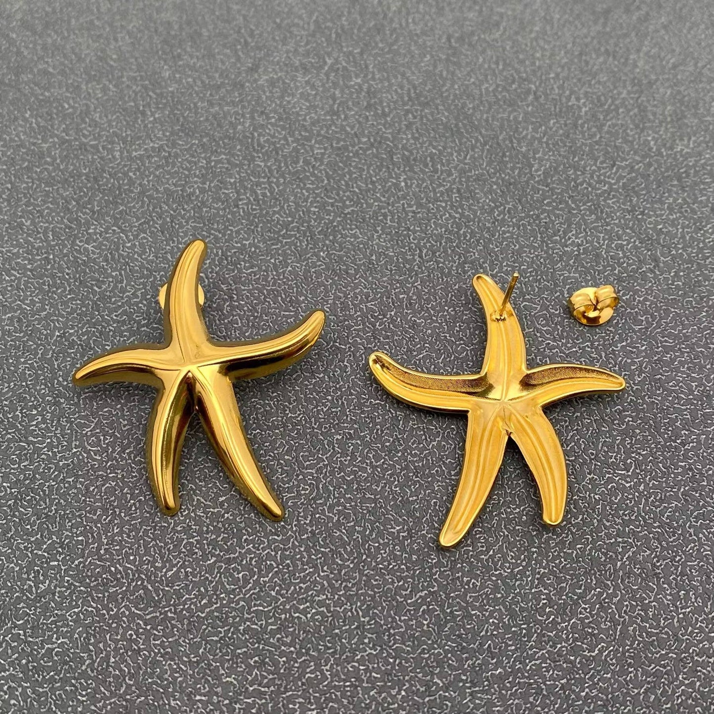 the front and back view of a pair of gold starfish stud earrings against a grey background