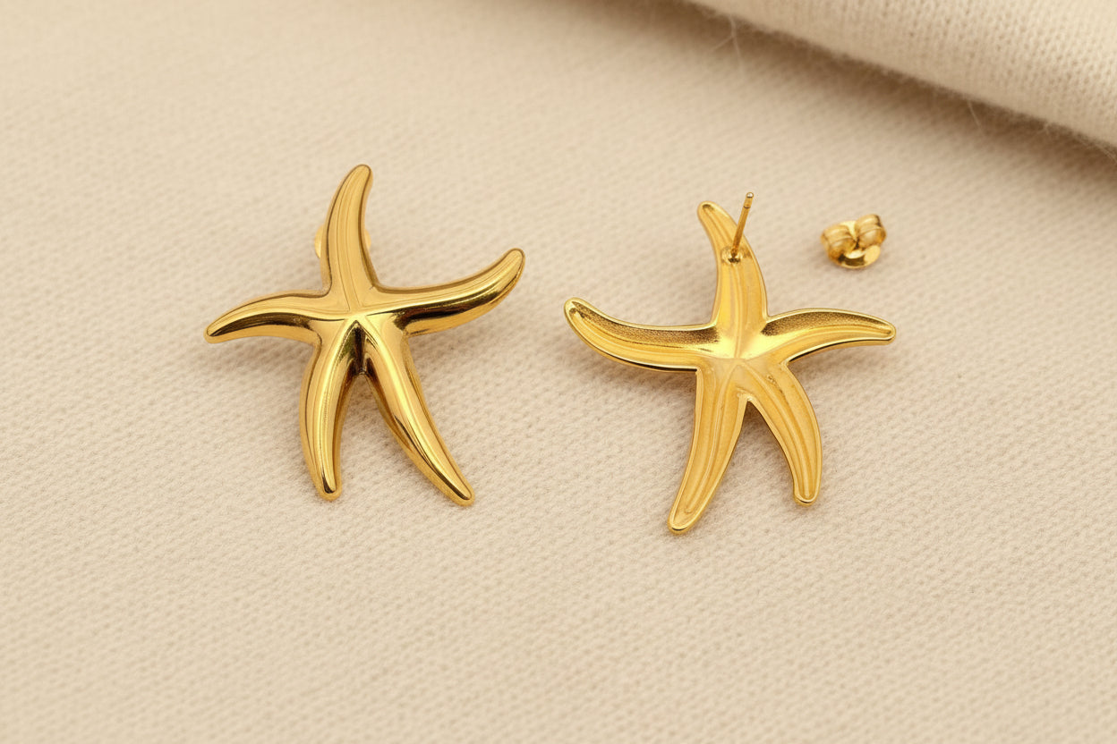 the front and back view of a pair of gold starfish stud earrings against an ivory fabric background