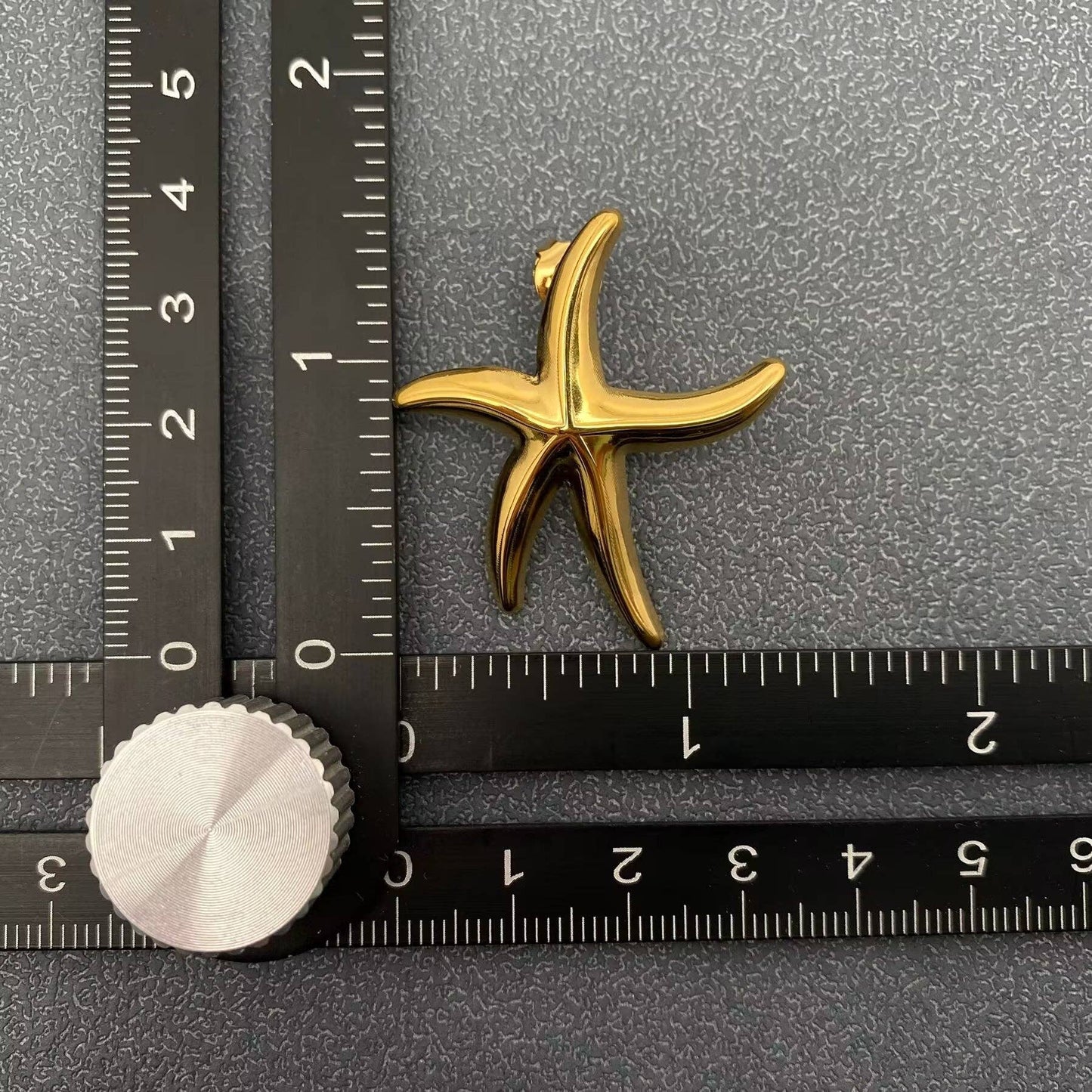 a gold starfish stud earring next to a ruler