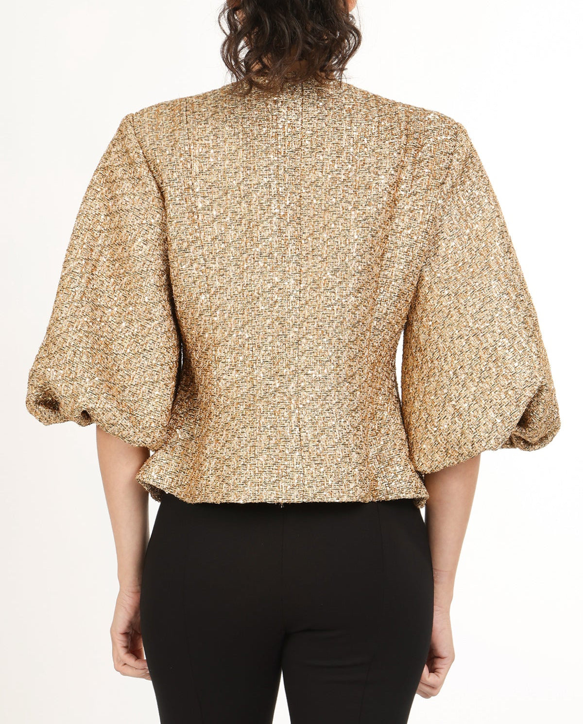 Back view of woman wearing a gold tweed puff sleeve jacket with black pants on a white background