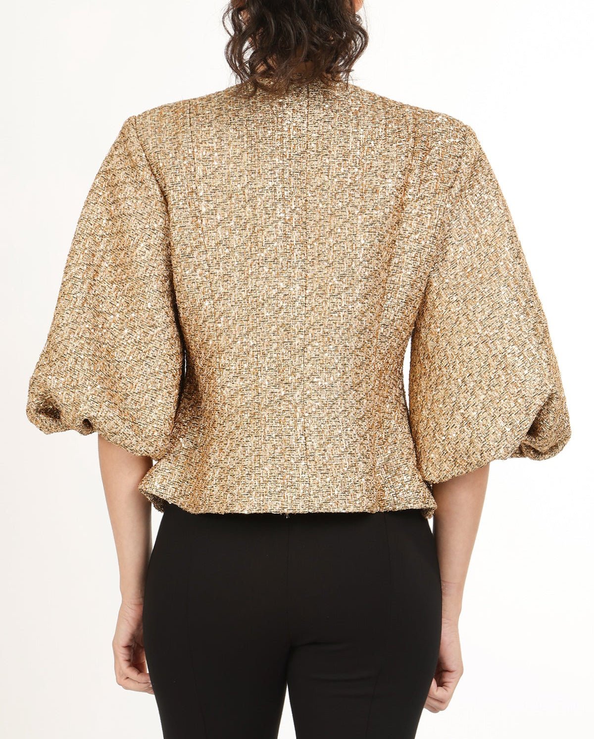 Back view of woman wearing a gold tweed puff sleeve jacket with black pants on a white background