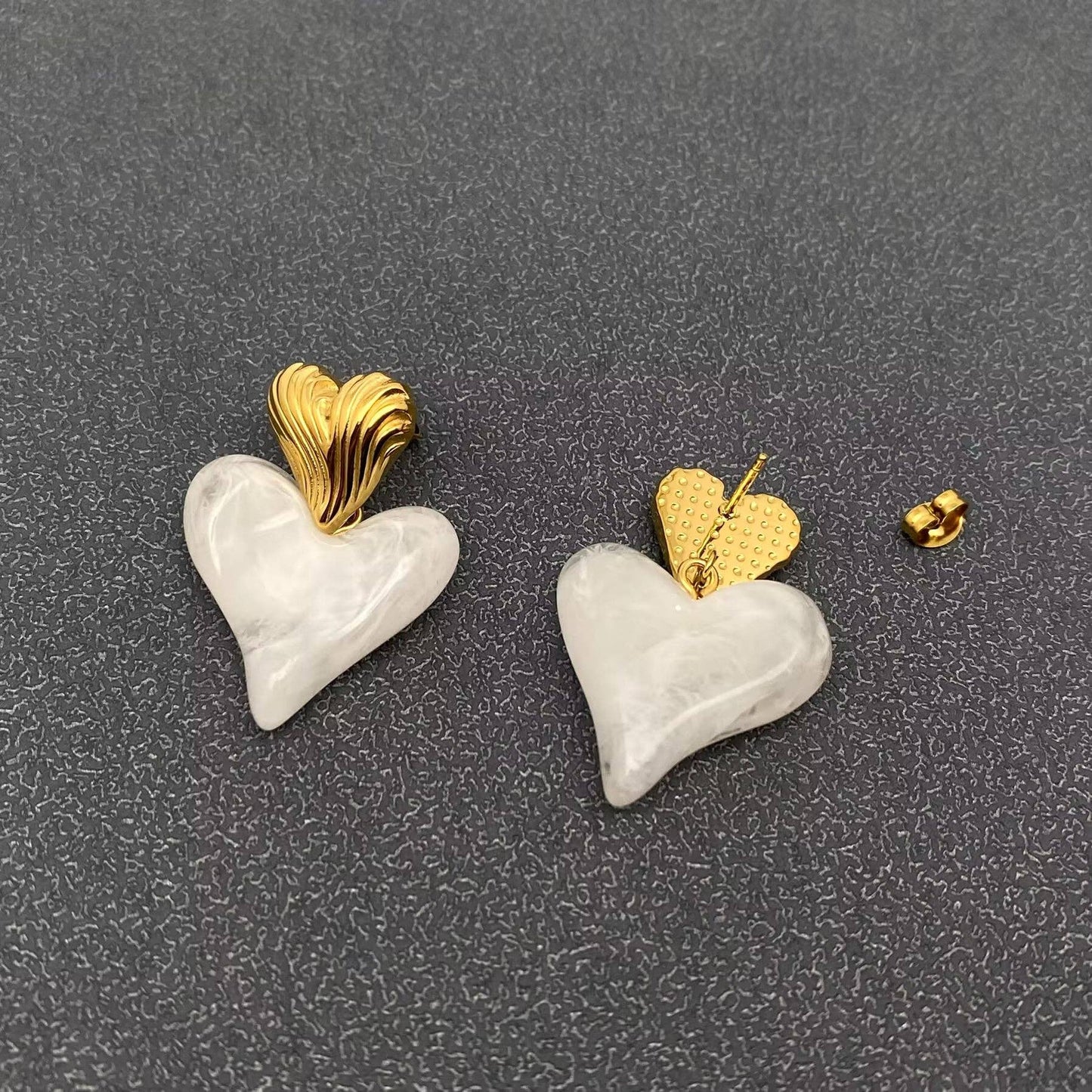 the front and back view of a pair of gold and white resin heart shaped dangle earrings against a grey background