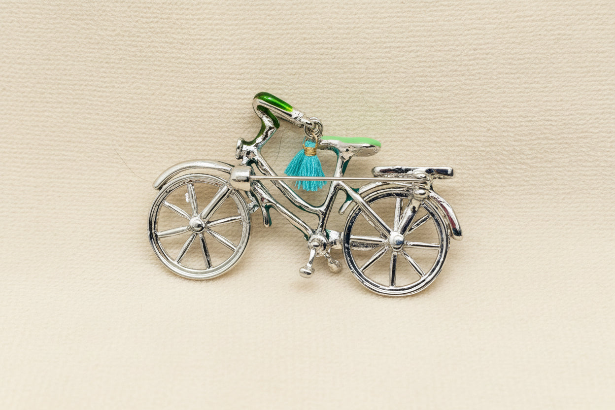 back view of bicycle charm with a green seat and blue tassel on a gray background