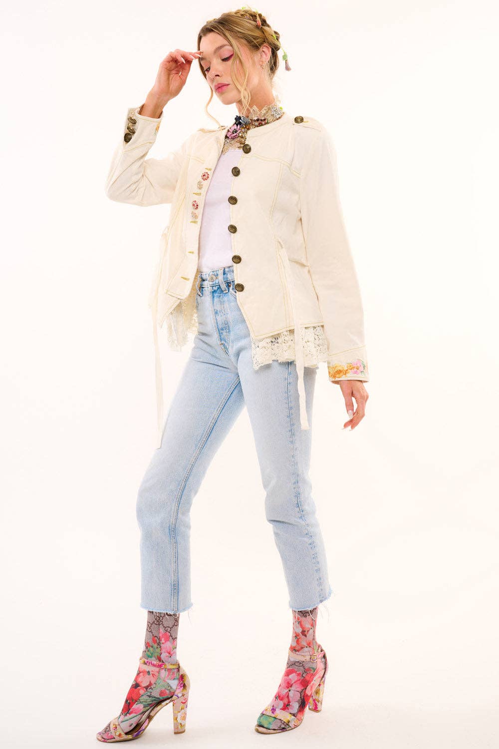 Woman wearing a cream jacket, light blue jeans, and floral shoes on a white background