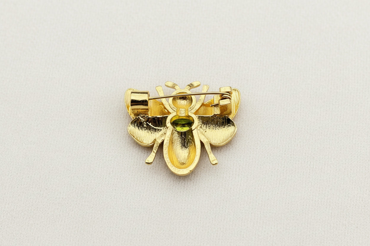 Back view of gold bee-shaped brooch to show pin closure on a textured gray background