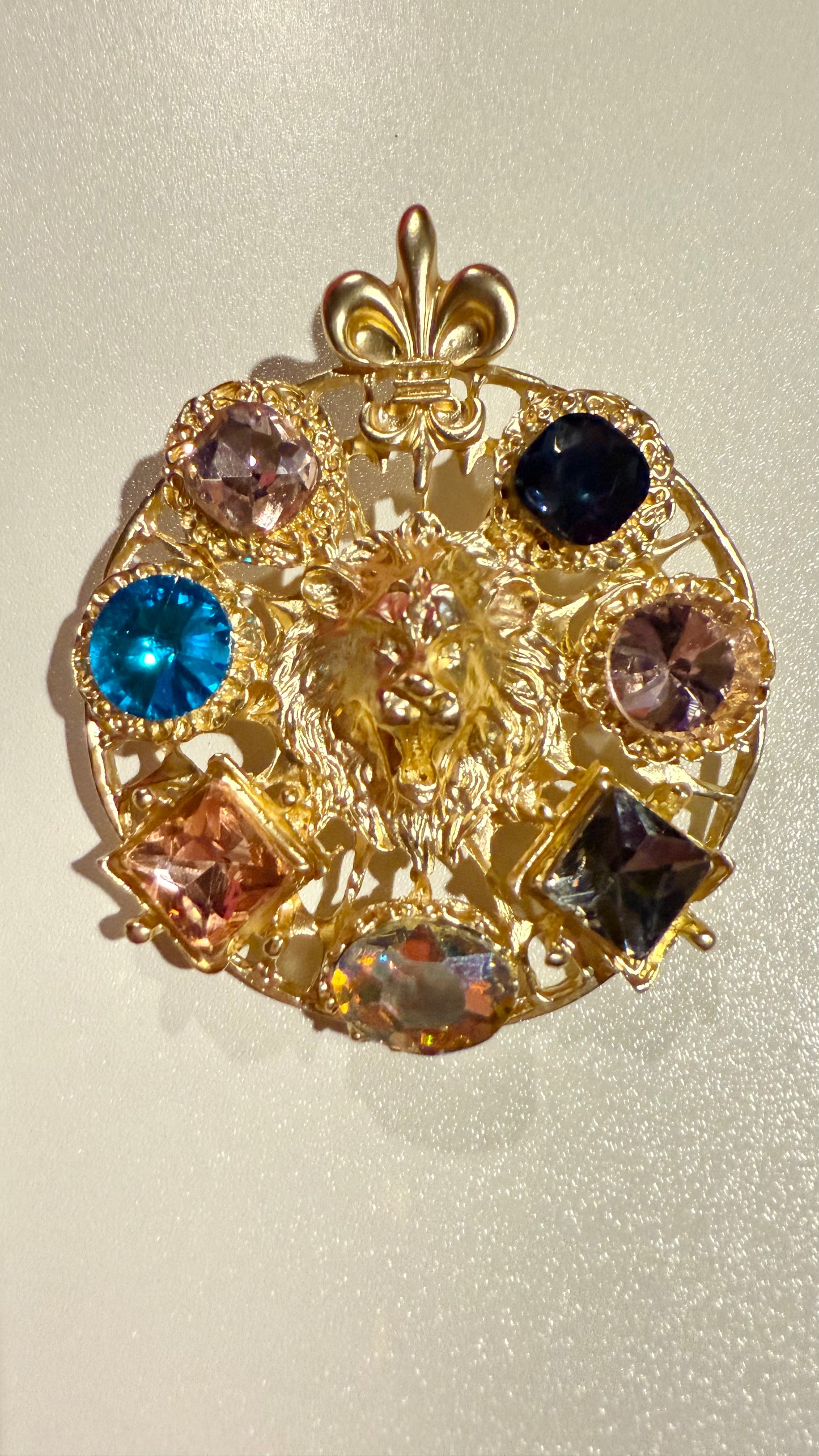 large round gold brooch with multi colored gemstones against a white background