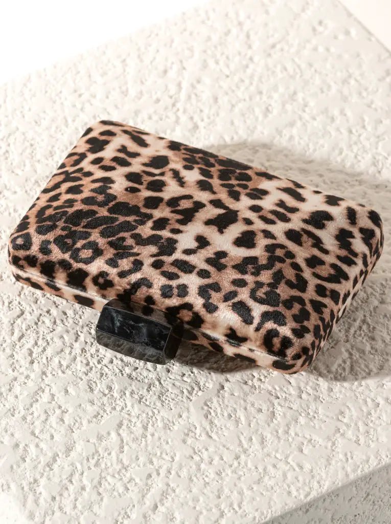 leopard print clutch bag with black resin closure laying on an ivory textured background