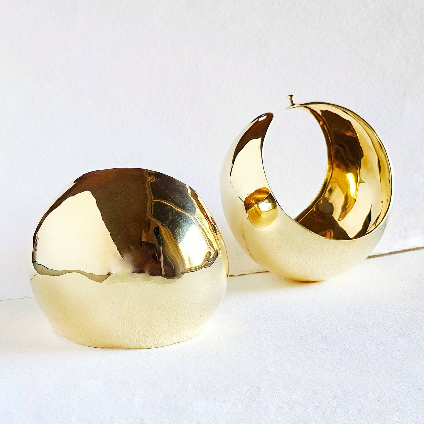 A pair of brass done shaped cuffs against a white background