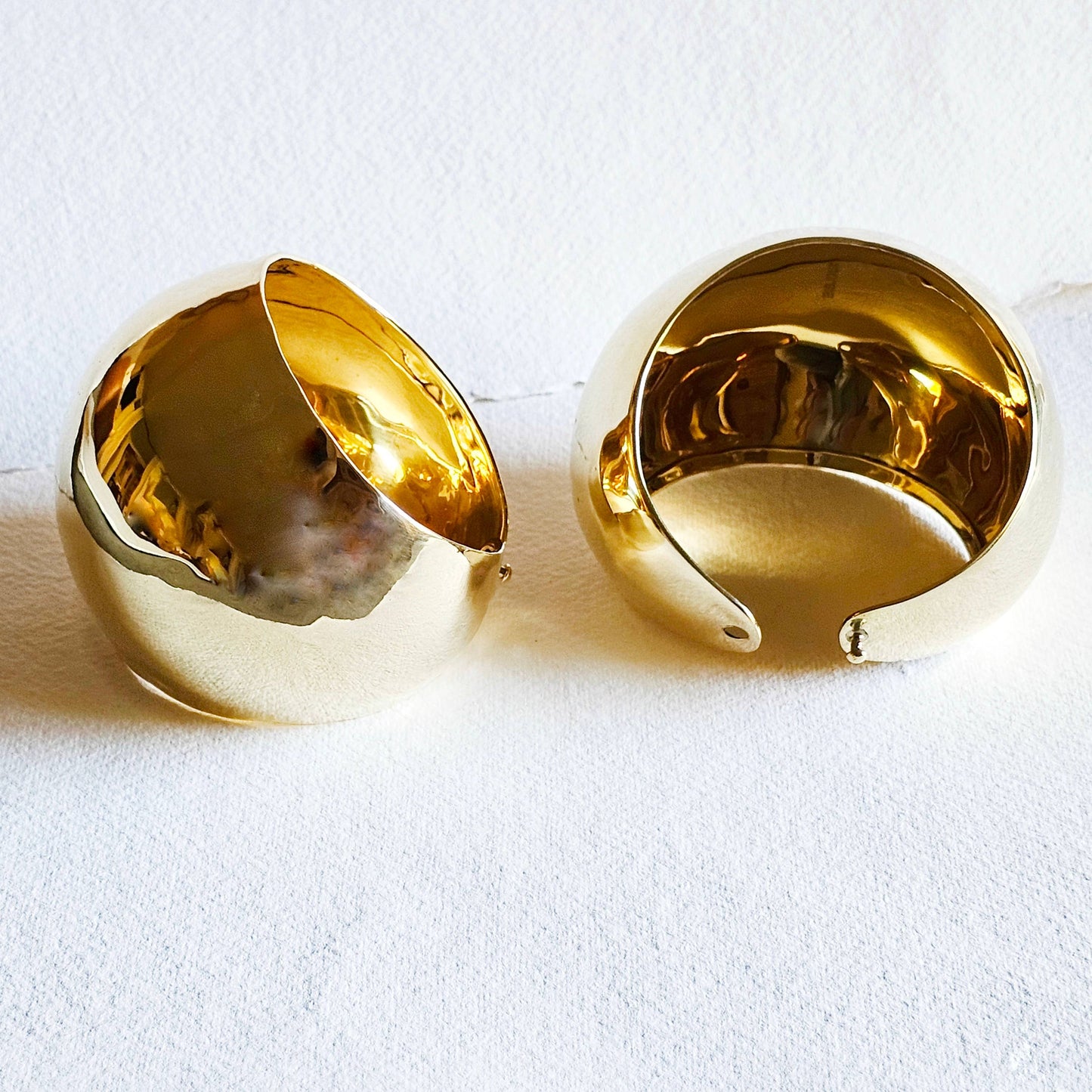A pair of brass dome shaped cuffs against a white background