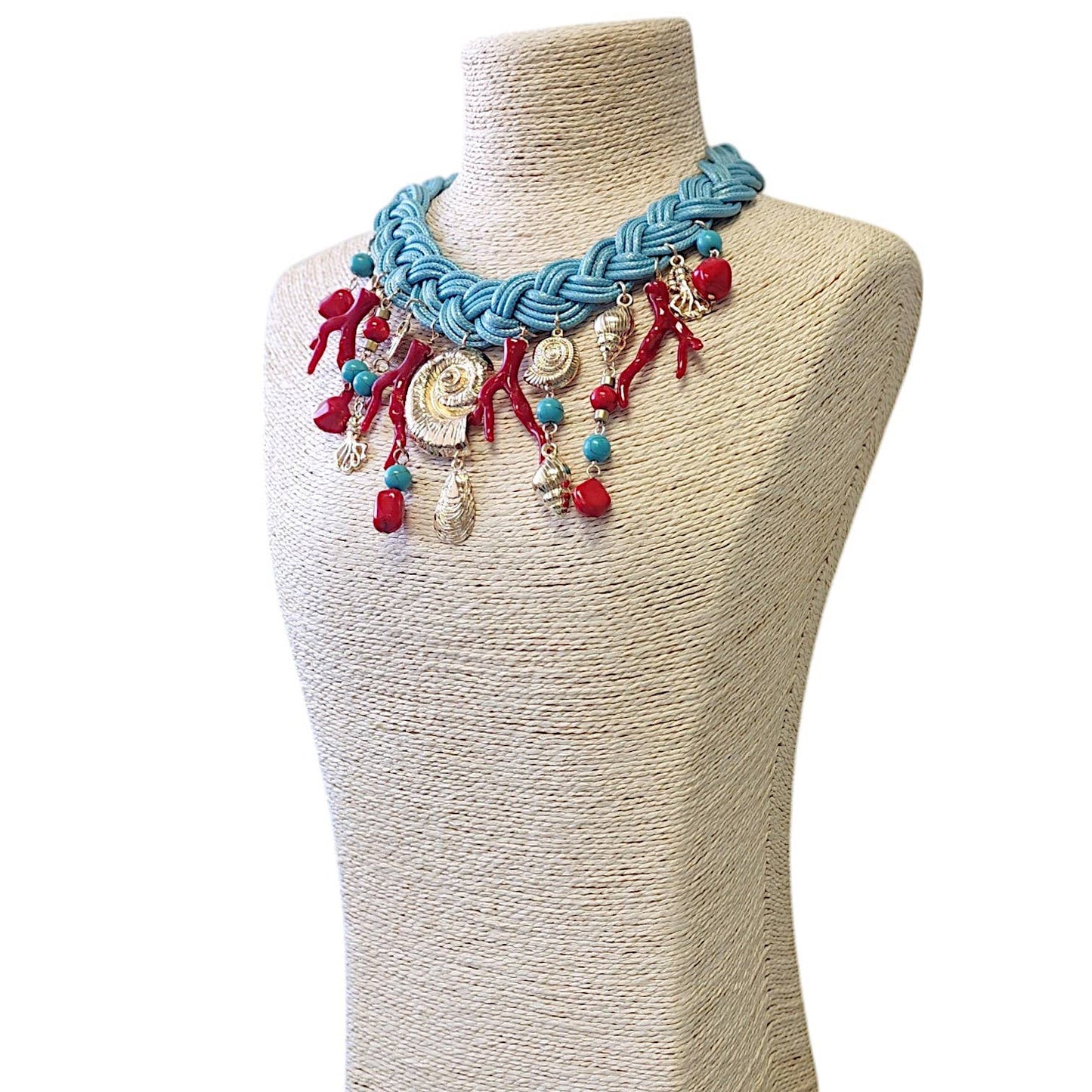 angled view of a turquoise, red, and gold charm necklace on a turquoise braided necklace on a mannequin