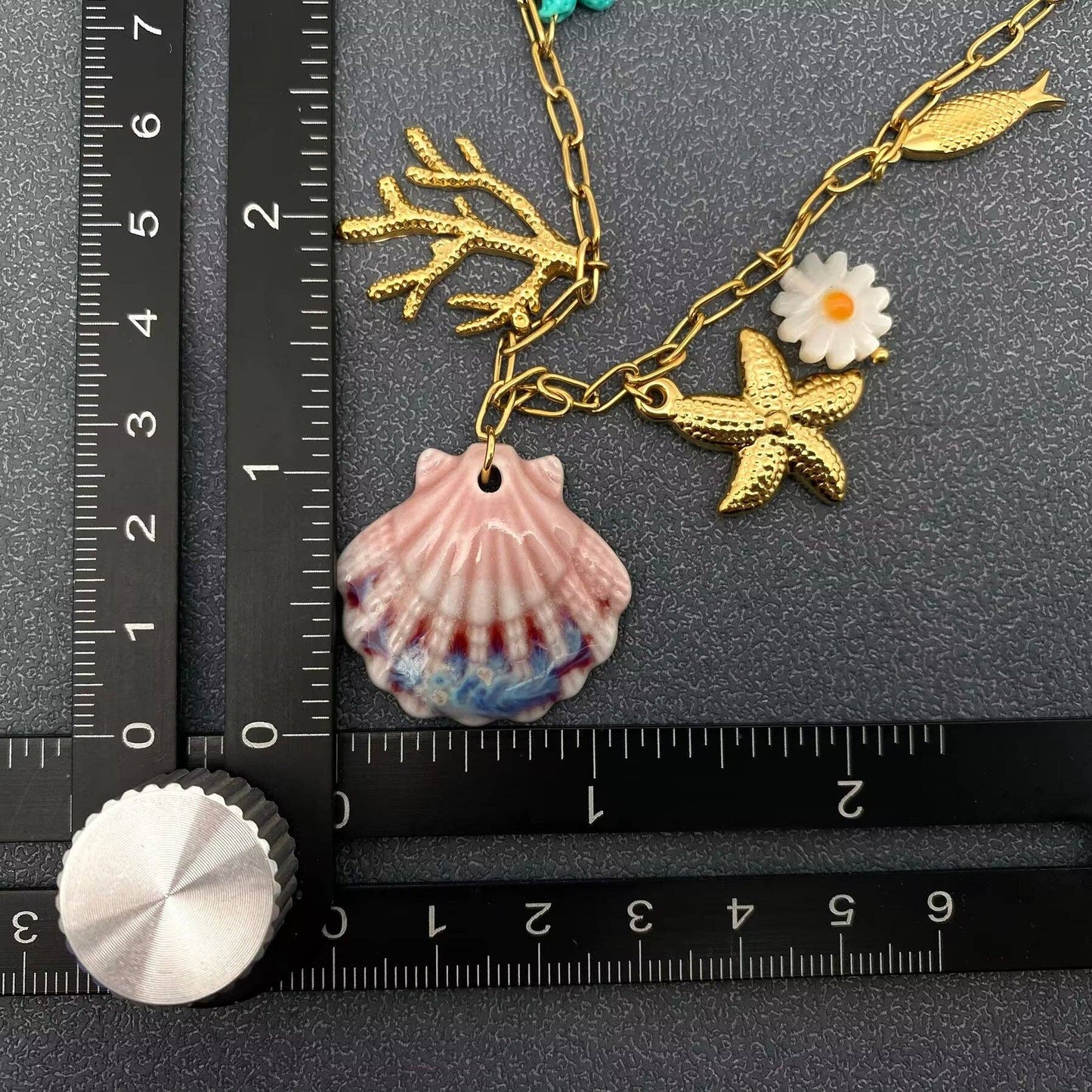 up close view of hand painted ceramic clam shells and some charms next to a black ruler against a grey background