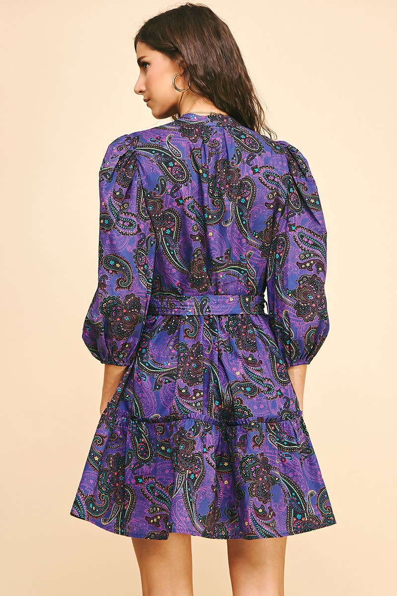 Back view of a woman wearing a purple paisley dress on a beige background