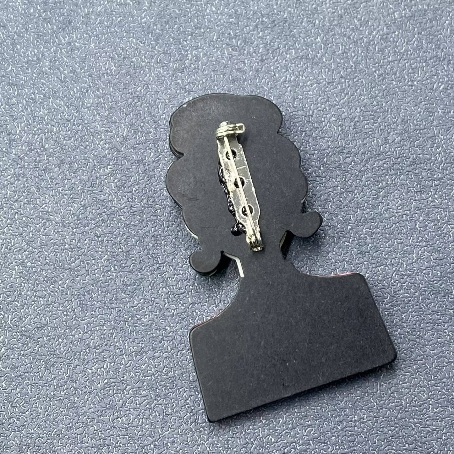 Back view of a silhouette of a person brooch to show pin closure on a textured gray background