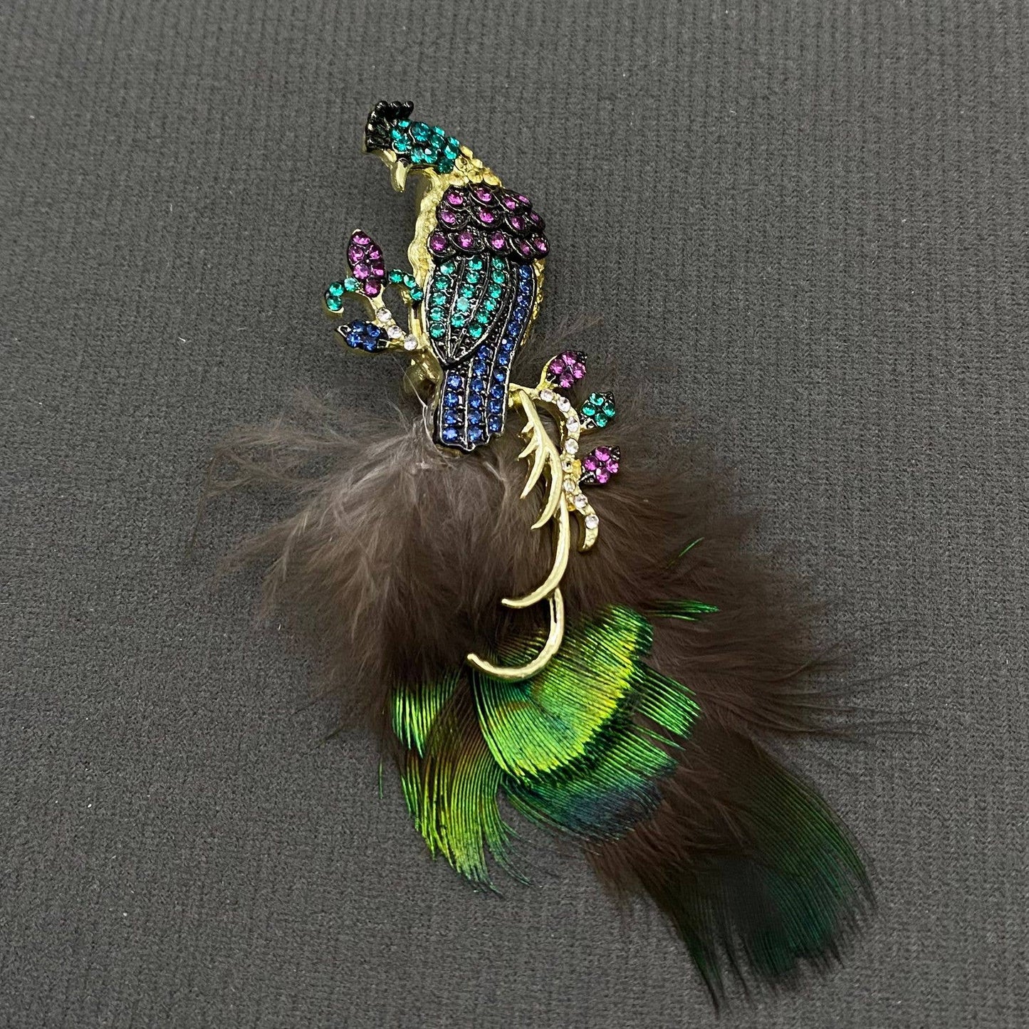 Decorative peacock brooch with feathers and gemstones on a gray background