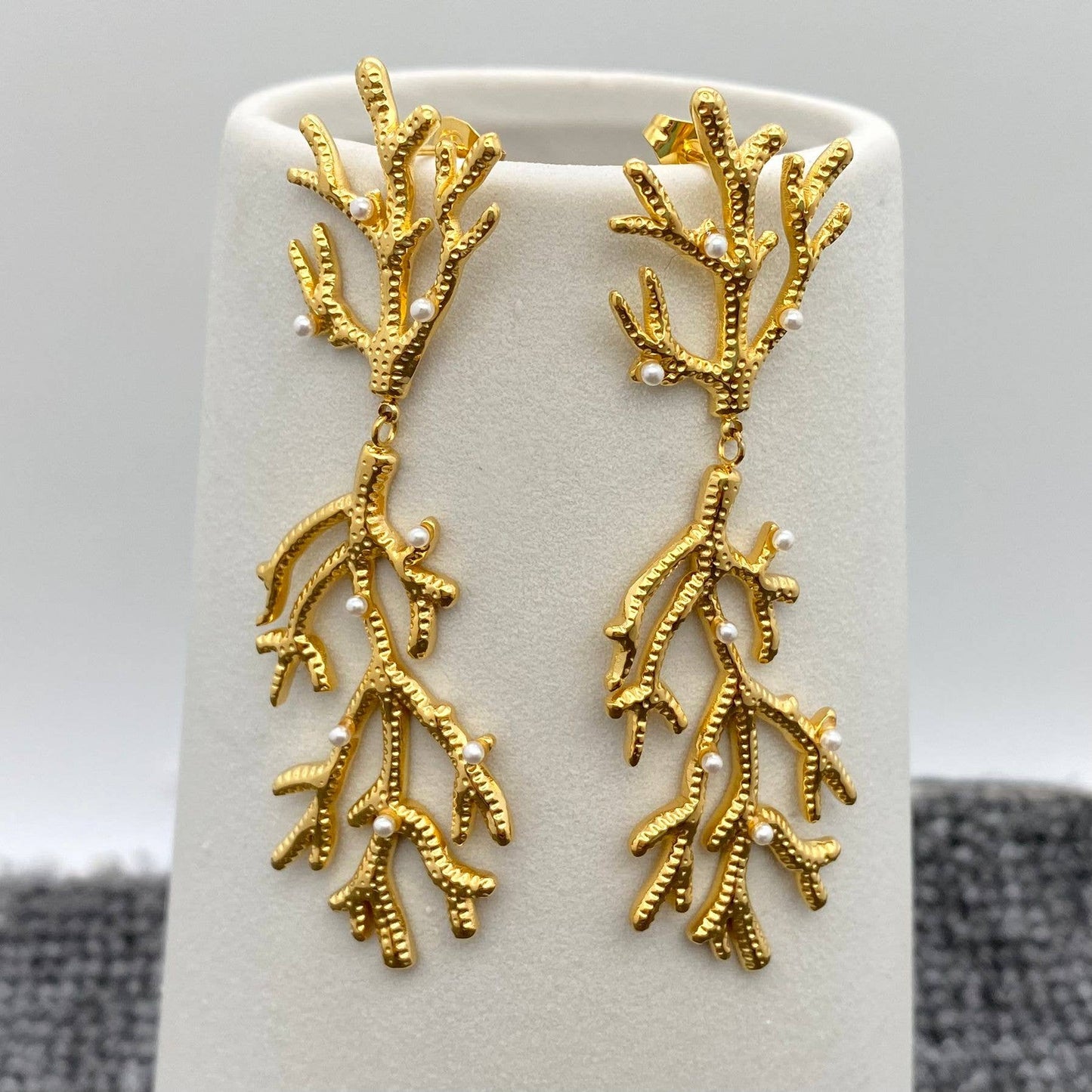 a pair of pearl encrusted gold coral shaped earrings on white stand