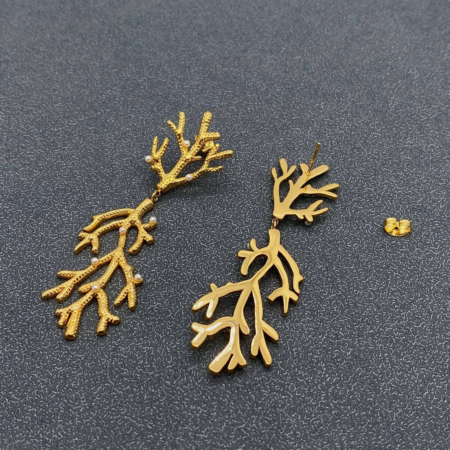 a pair of gold pearl encrusted earrings with one turned on its back laying on a grey surface