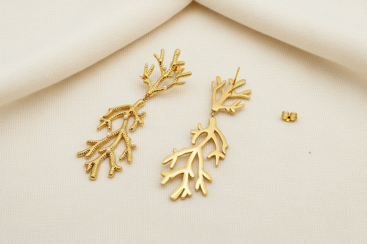 a pair of gold pearl encrusted earrings with one turned on its back laying on an ivory surface