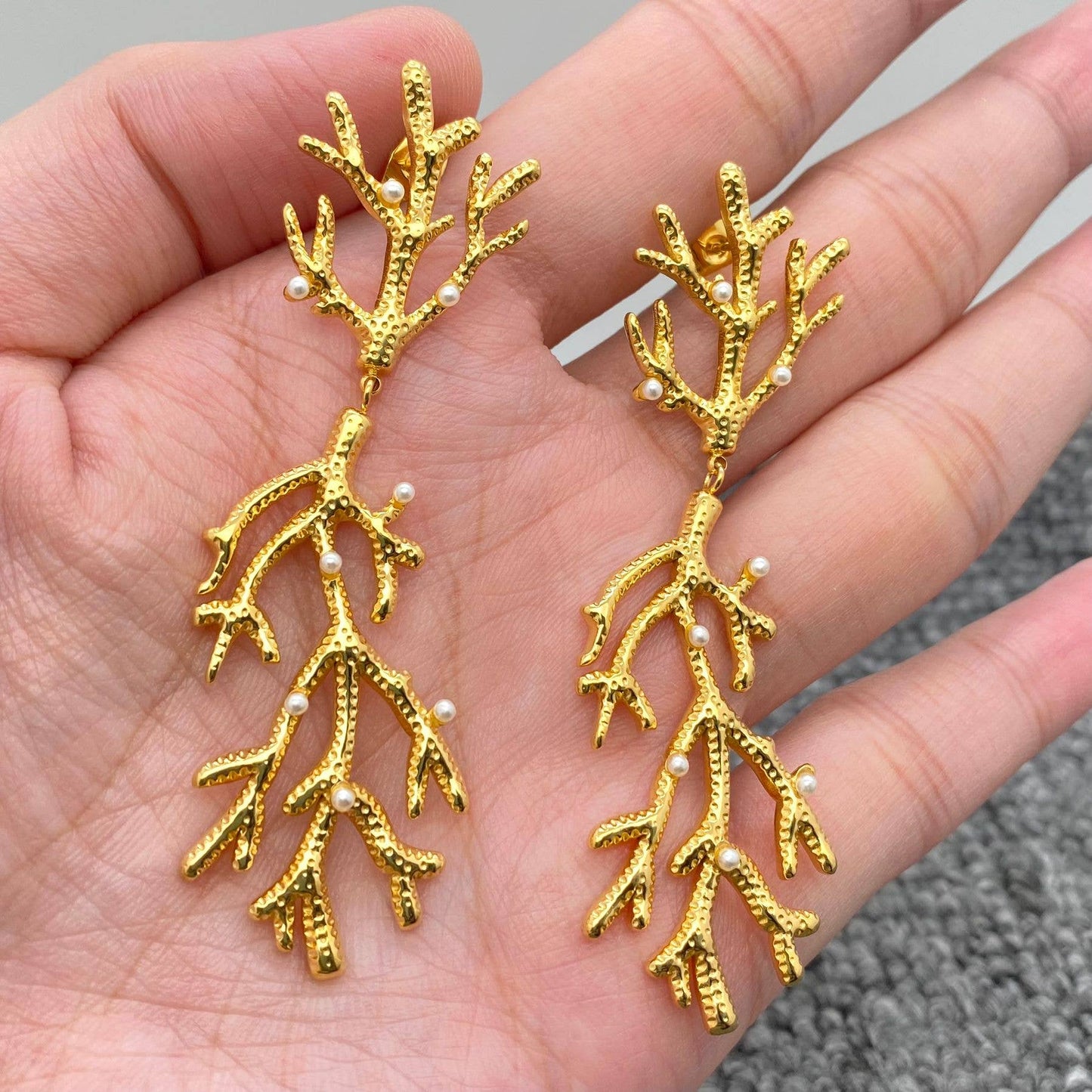 a pair of gold pearl encrusted coral shaped earrings in a palm of a hand