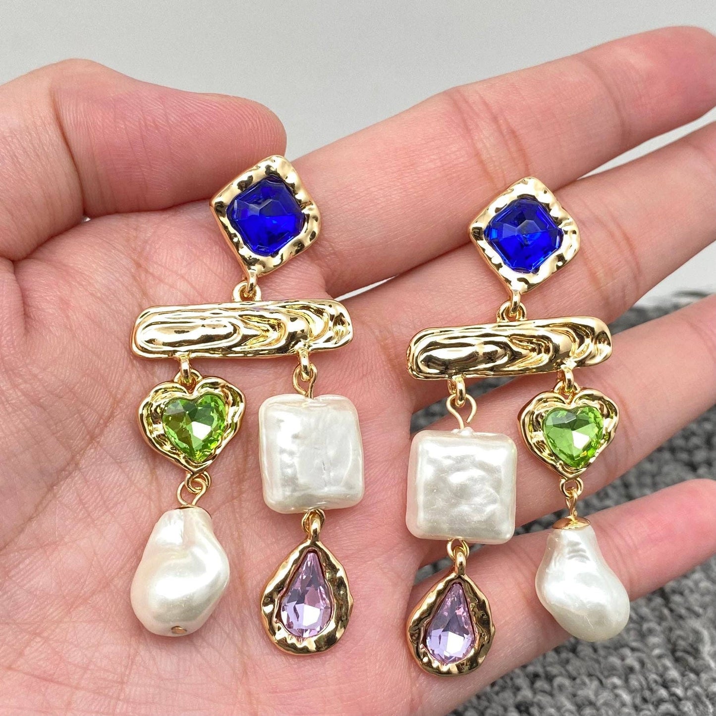 Hand holding multi-stone pearl drop earrings in blue tones with baroque pearls and colored stones