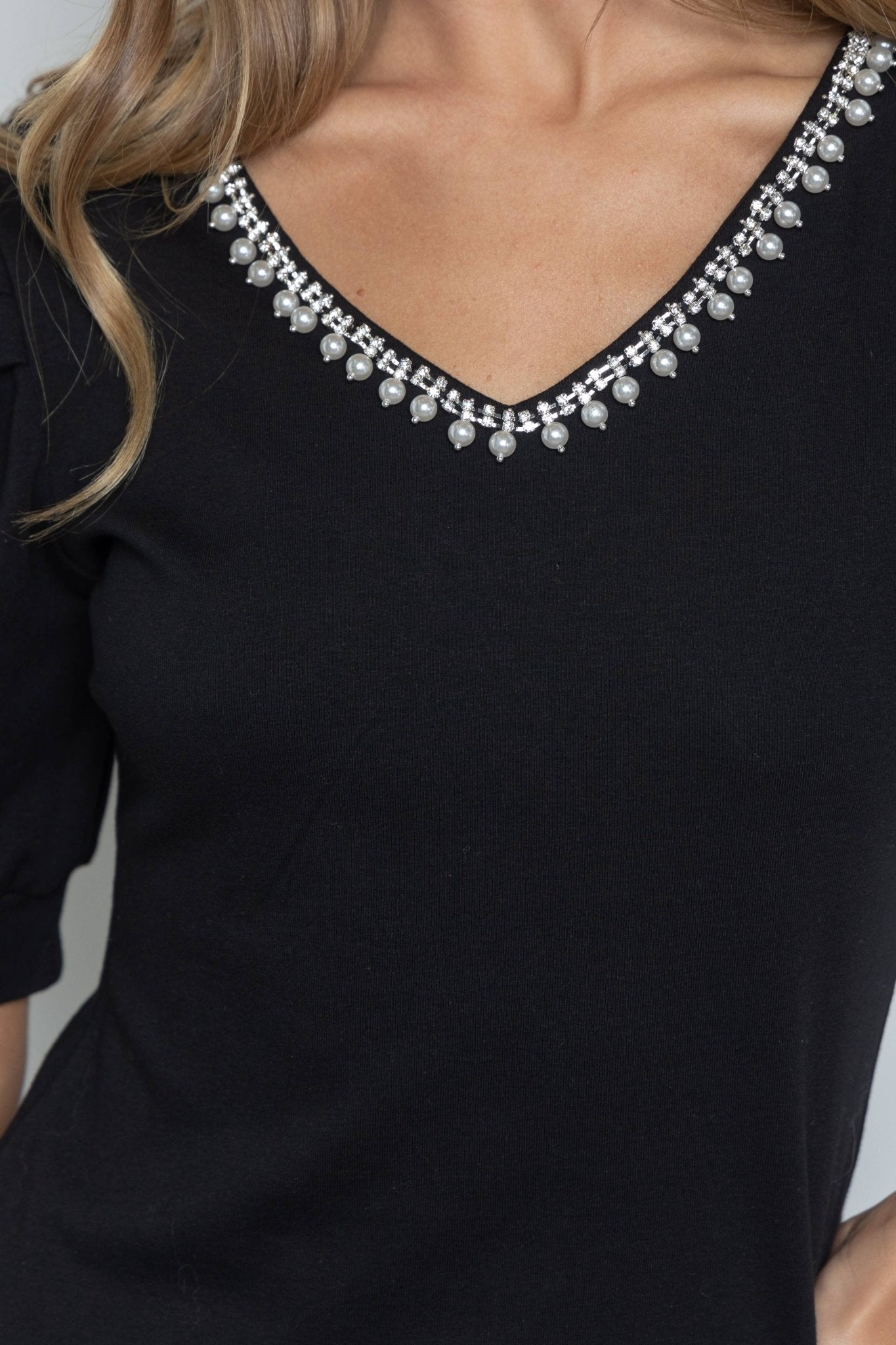 Black top with decorative neckline against a neutral background