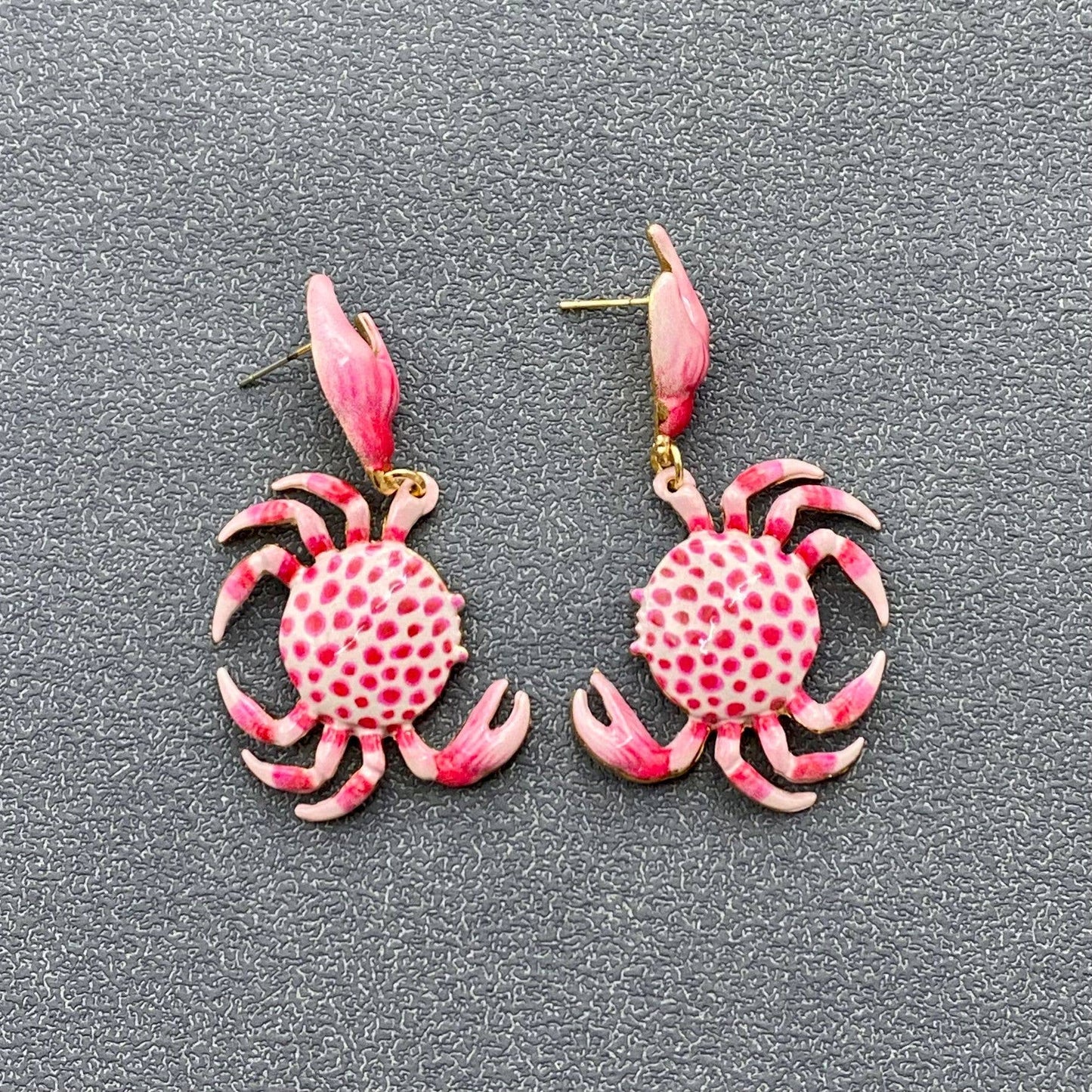 a pair of pink and white crab dangle earrings on grey background