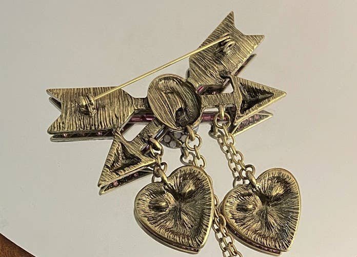 back view of a heart and arrow brooch showing the pin closure on a mirrored surface