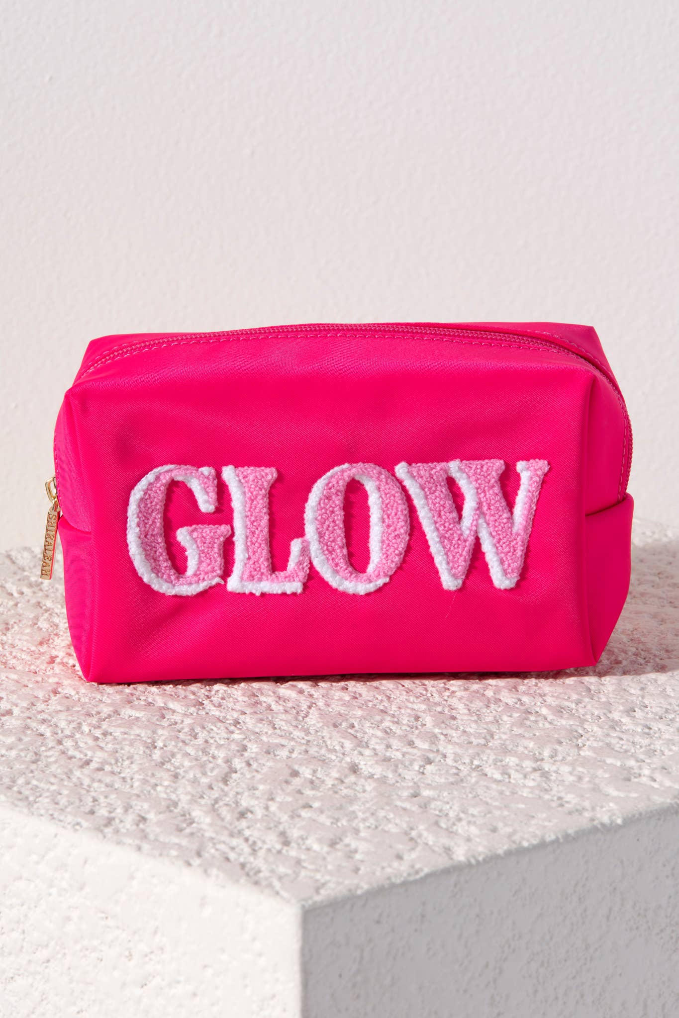 Pink cosmetic bag with 'GLOW' text on an ivory textured surface