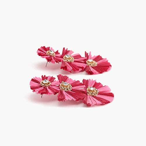 side view of a pair of pink and red raffia earrings laying on a white background