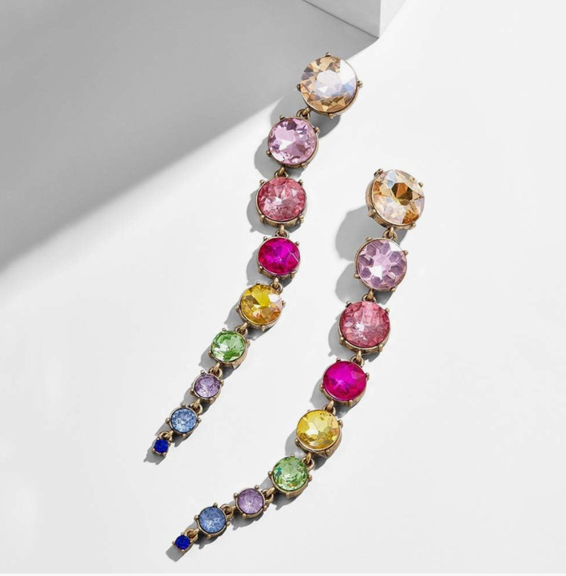 a pair of rainbow colored crystal drop earrings with round cubic zirconia stones against a white background