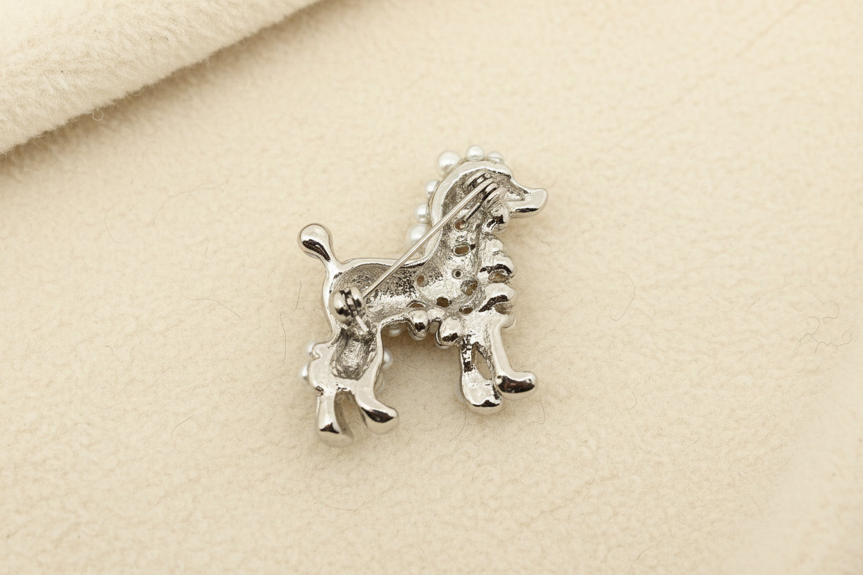 Back view of dog-shaped brooch in a silver color on a textured gray background