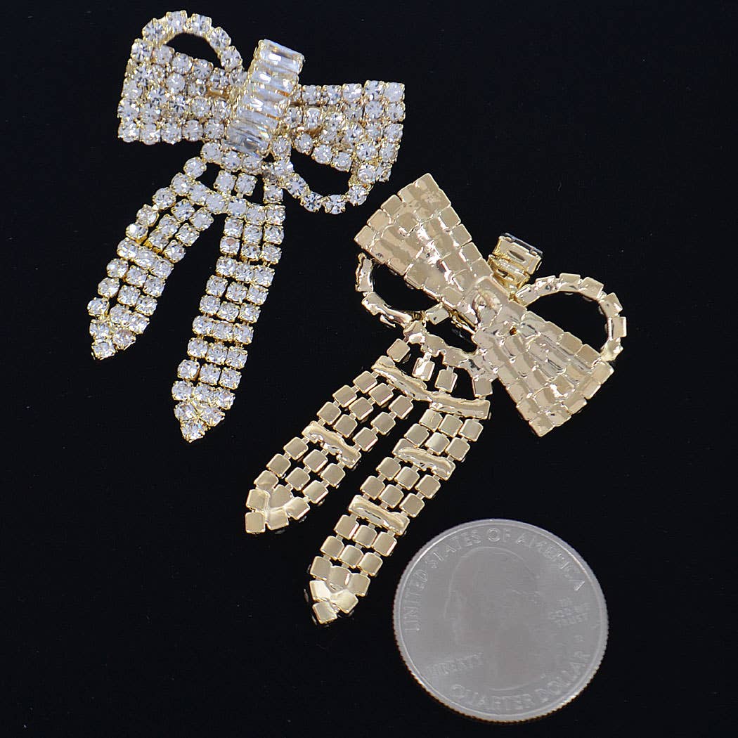 a pair of ribbon shaped rhinestone earrings next to a quarter to show the size reference