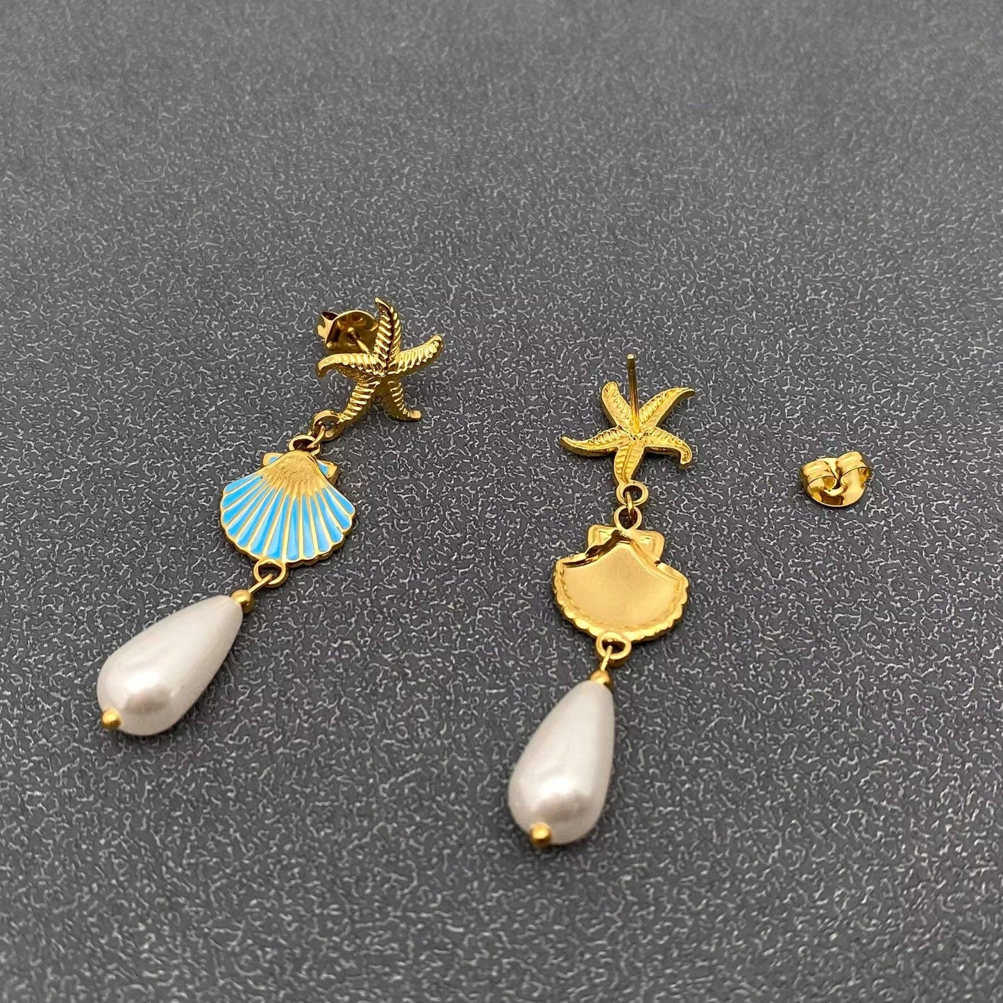 front and back view of coastal inspired gold earrings with gold starfish, enamal clam and pearl drop