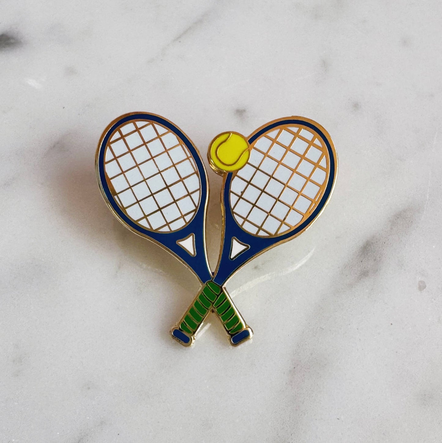 Pin with two crossed tennis rackets and a yellow ball on a marble background