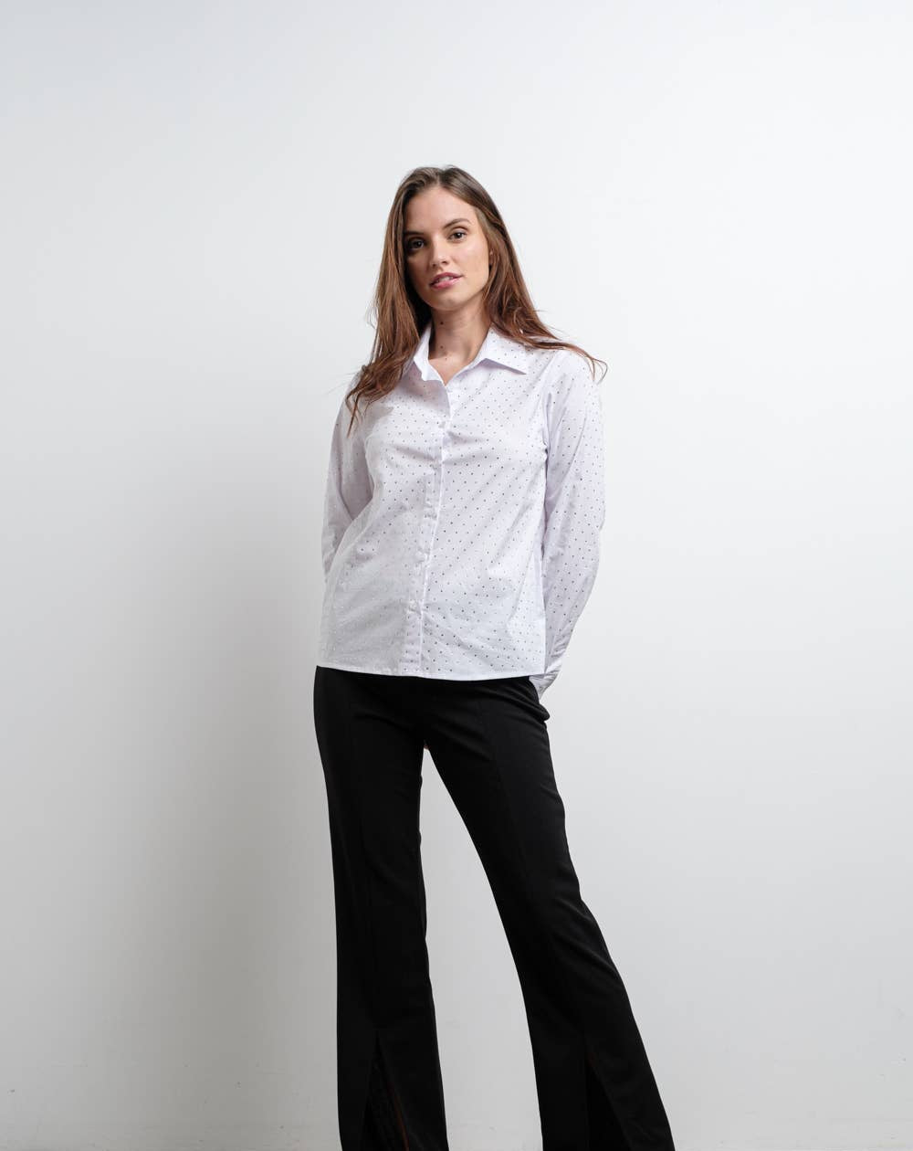 Woman wearing a white shirt and black pants against a plain background