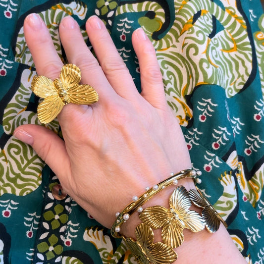 a woman's head wearing a gold butterfly ring, butterfly cuff, and crystal bangle against green patterned fabric