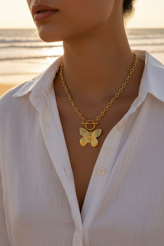 Woman with a white button down blouse and gold butterfly toggle necklace outside near the beach