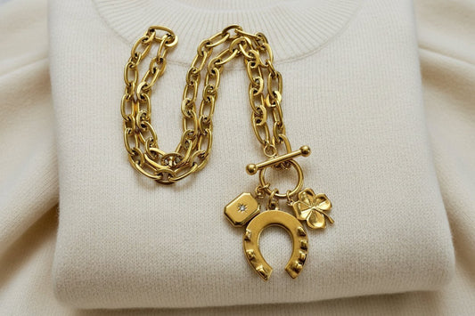 gold charm necklace guide featuring a chain link necklace with horseshoe and clover charms against an ivory sweater