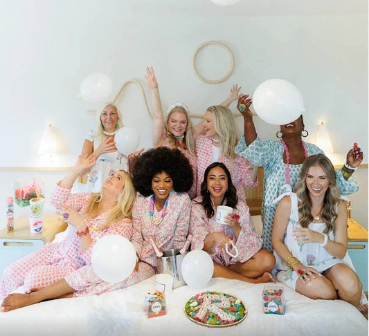 Charleston Gift Guide featuring women wearing pajamas with candy, candles, and balloons on a bed together