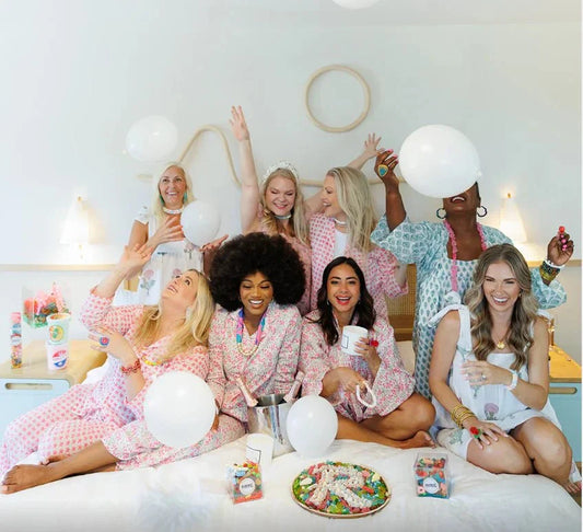 Charleston Gift Guide featuring women wearing pajamas with candy, candles, and balloons on a bed together