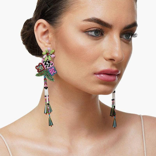 A woman earing beaded statement earrings with fringe detail against a white background