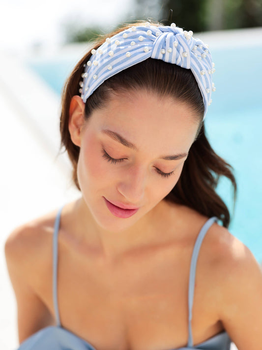Woman wearing a blue and white stripe headband with pearl embellishments in an outdoor setting