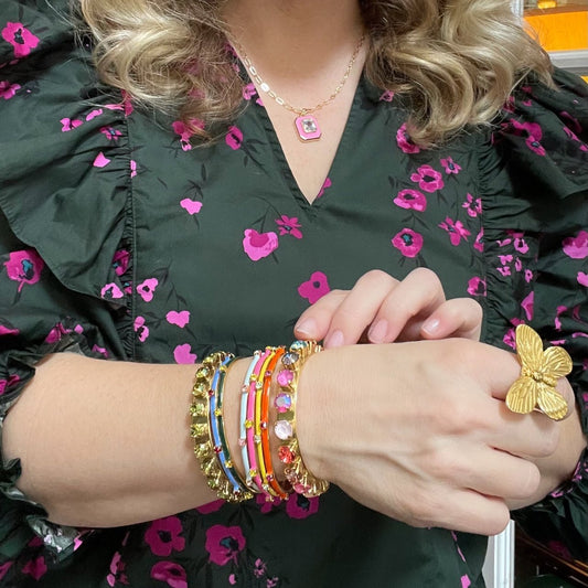 Woman in a green & pink floral blouse wearing various crystal cuff bracelets in multiple colors and a gold butterfly ring