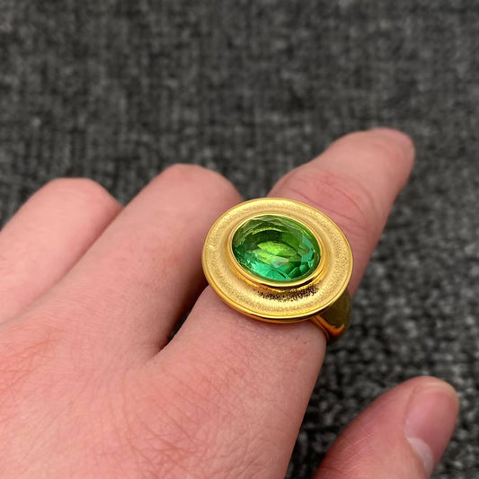 Hand wearing a gold ring with center oval emerald stone