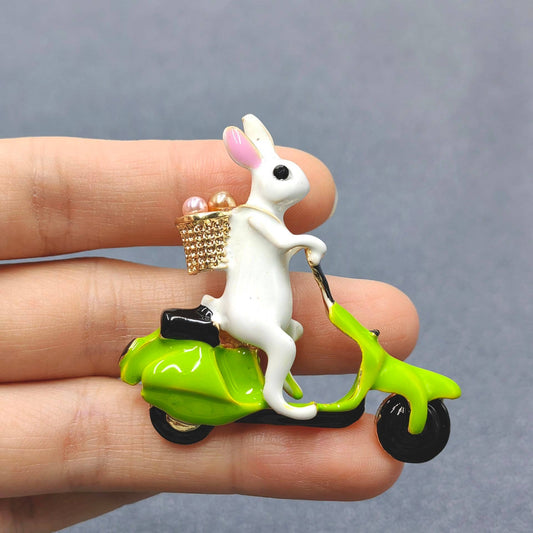 A rabbit on a green scooter brooch in a person's hand 