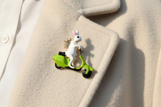 An enamel bunny rabbit riding a green scooter brooch on an ivory wool coat lapel