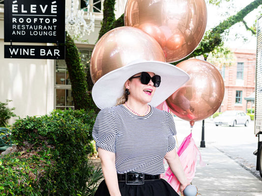girl holding gold balloons smiling and walking down the street