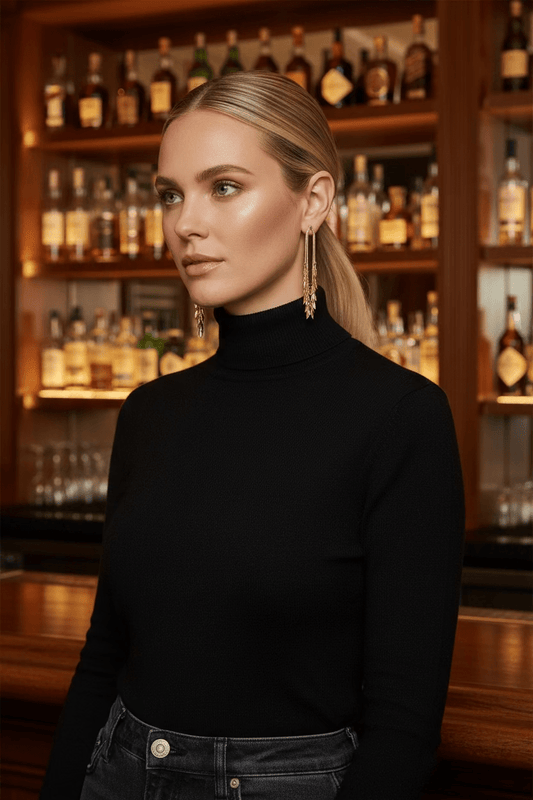 One pair of earrings: Five Outfits featuring a woman wearing gold leaf fringe dangle earrings and a black turtleneck in a luxury bar setting